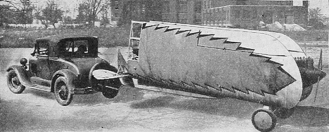Figure 7 — A Heath Parasol with its wings folded back, being towed behind a car, as shown in Aero Digest in July 1930. Removable wings let a Parasol owner keep the aircraft in a garage rather than pay for a h…