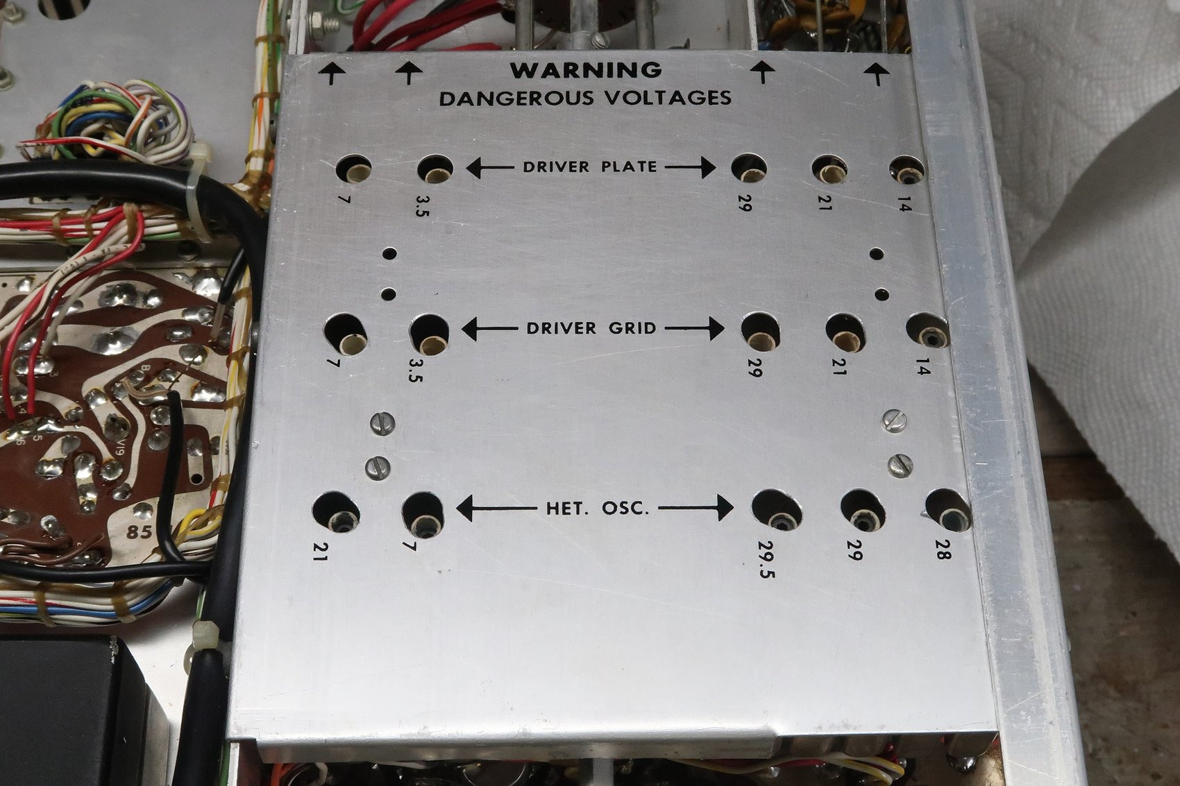 Figure 9 — A coil cover with its access holes eased so that the coils beneath can actually be adjusted with the cover fitted. The "WARNING — DANGEROUS VOLTAGES" legend is the factory's, and it means it.
